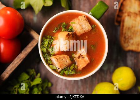 A top view of a Tomato soup with bread pieces in it filled in a large bowl on a wooden table Stock Photo