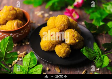 Un gros plan du dessert Laddu avec de la farine de pois et des noix sur une assiette décorée de légumes verts sur une table en bois Banque D'Images