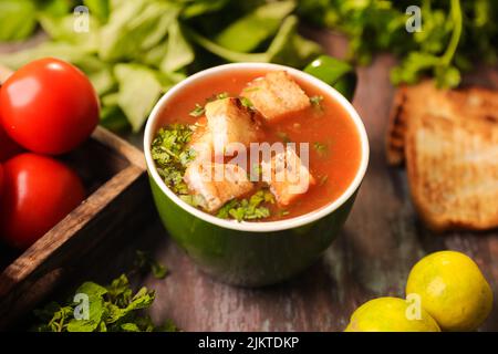 Un gros plan d'une soupe de tomates avec des morceaux de pain dans elle rempli dans un grand bol sur une table en bois Banque D'Images