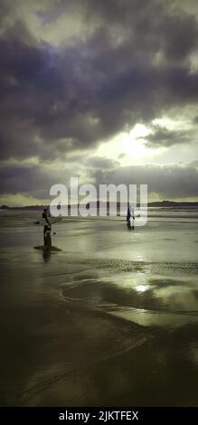 Une vue verticale du soleil qui brille derrière des nuages sombres sur les surfeurs de la plage Banque D'Images