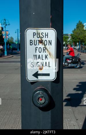 A vertical shot of a metal sign with Push button for walk signal and a red button on grey metal column Stock Photo