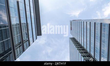 A low-angle shot of two modern glass buildings rising up to the blue sky in an urban area Banque D'Images