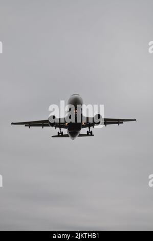 A vertical low angle grayscale shot of a plane flying in the sky Stock Photo