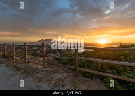 A view of the golden sun setting in a deep blue cloudy sky from behind a wooden face in Blouberg near Cape Town Stock Photo