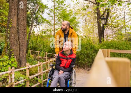 Un jeune homme paralysé en fauteuil roulant, poussé par un ami dans un parc public de la ville, regardant le paysage Banque D'Images