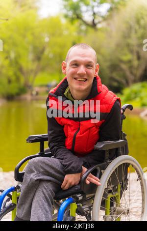 Portrait d'un jeune homme paralysé dans un parc public de la ville. Assis dans le fauteuil roulant souriant en regardant la caméra Banque D'Images