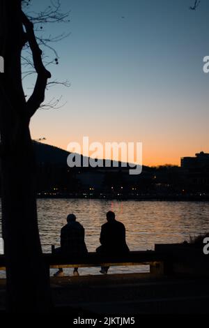 The silhouette of two people sitting on the bench on the coast at sunset Banque D'Images