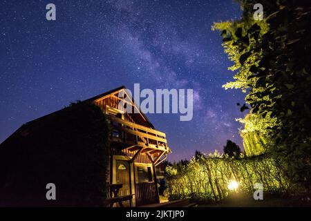 A view of a cozy small house with green bushes and trees in front of it under a srarry sky Stock Photo