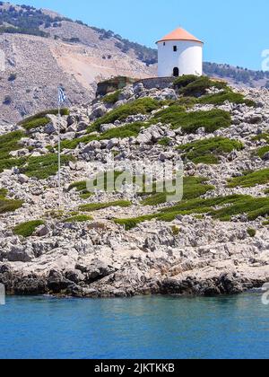 SYMI, GRÈCE - 09 JUILLET 2021 : le moulin à vent qui vous accueille à l'entrée du port au monastère de la ville grecque de Symi. Banque D'Images