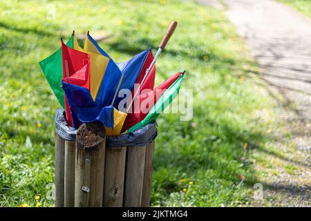 A closeup of a broken multicolor umbrella thrown in a trash can. Stock Photo