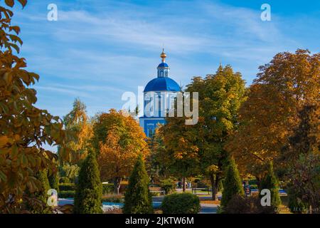 The dome and cross of a church seen between colorful trees and against blue sky in autumn in Russia Banque D'Images