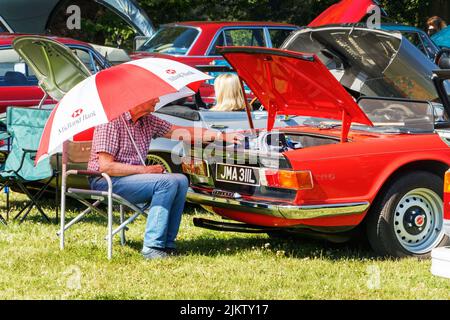 Homme avec parapluie rayé assis à l'arrière de Triumph rouge vintage TR6 voiture de sport britannique 1972 Inscription JMA 311L au salon de voiture de stationnement weston Banque D'Images