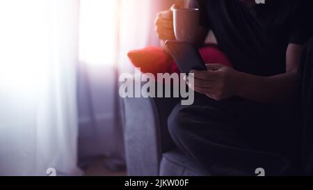 Beau jeune hispanique à la maison de boire du café et à l'aide de son smartphone Banque D'Images
