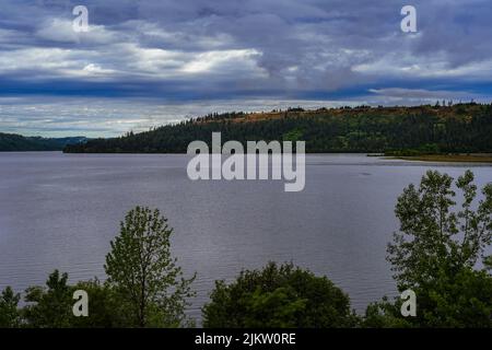 A beautiful landscape view of Coeur D'Alene River and a tree lined ridge outside against cloudy sky in Harrison, Idaho, United States Stock Photo