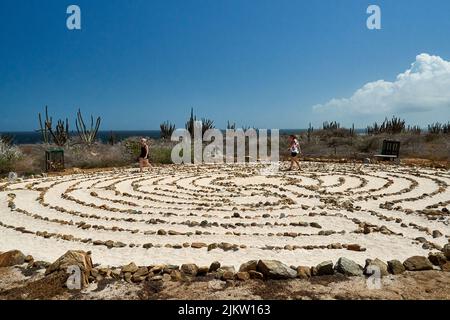 Deux dames marchant dans le labyrinthe sableux de la paix d'Aruba à l'église Alto Visto avec une vue sur l'océan, cactus et un ciel bleu vif. Banque D'Images