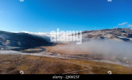 Photo aérienne de montagnes enneigées brumeuses au-dessus de la vallée sur fond bleu ciel Banque D'Images