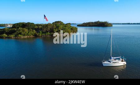 An aerial view of small yacht in ocean and American flag surrounded by green trees Banque D'Images