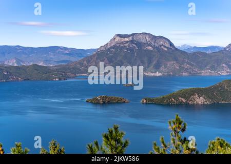 An aerial view of Lugu Lake in China surrounded by rocky mountains in blue sky background Stock Photo