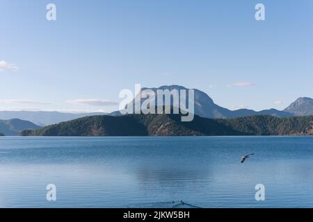 An aerial view of Lugu Lake in China surrounded by rocky mountains in blue sky background Stock Photo