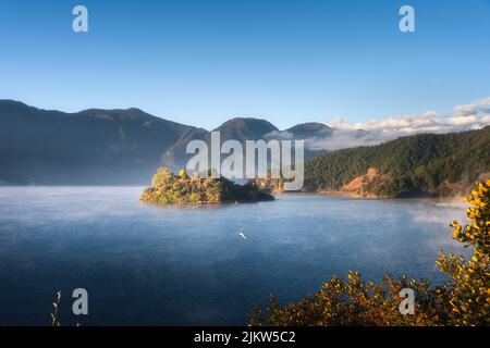 An aerial view of Lugu Lake in China surrounded by rocky mountains in blue sky background Stock Photo