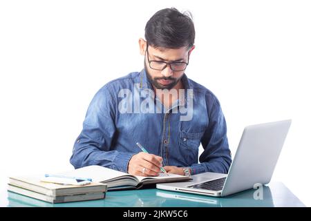 un jeune homme d'affaires écrit sur un bloc-notes ou un journal tout en travaillant sur un ordinateur portable ou un ordinateur Banque D'Images
