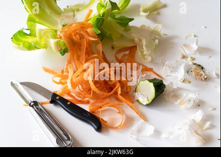 Une vue de dessus des pelures de carottes, de la laitue et des couteaux sur une table blanche Banque D'Images