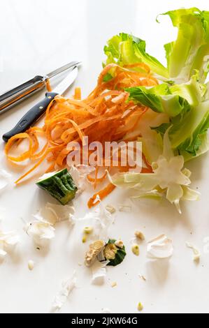 A vertical shot of carrot peels, lettuce, and knives on a white table Stock Photo