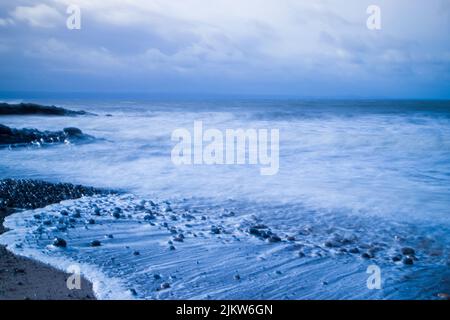 A scenic view of ocean waves crashing against the rocky beach on a cloudy day Stock Photo