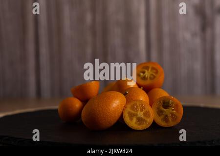 Gros plan de petites oranges chinoises ou Kumquat (Citrus sinensis) sur une tuile noire sur une table en bois Banque D'Images