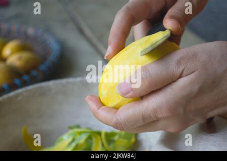 Femme utilisant un couteau pour peler la mangue mûre. Les fruits locaux sont doux. Banque D'Images