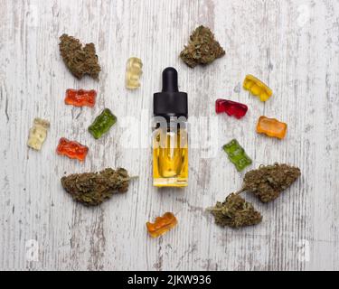 Une bouteille en verre avec de l'huile de CBD de cannabis jaune se trouve sur une table en bois entourée de bourgeons de marijuana médicale secs et d'ours en gelée de cbd colorés Banque D'Images