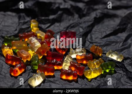 Les ours en gelée multicolores reposent de manière chaotique sur un matériau noir froissé Banque D'Images