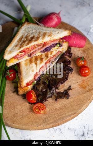 sandwich de deux toasts de pain avec farce et légumes sur une planche en bois vue du dessus. Banque D'Images