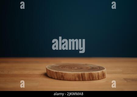 A piece of cut wood on a wooden surface in front of a dark blue background Stock Photo