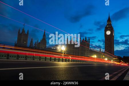 Des pistes rouges capturées au crépuscule en juillet 2022 tandis que des véhicules passent le pont de Westminster et se trouvent en direction de Big Ben. Banque D'Images