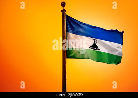 Le drapeau national du Lesotho sur un mât isolé sur fond orange Banque D'Images