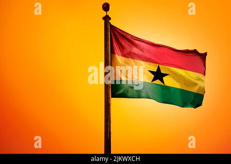 The national flag of Ghana on a flagpole isolated on an orange background Stock Photo