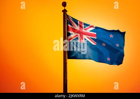 The national flag of New Zealand on a flagpole isolated on an orange background Stock Photo