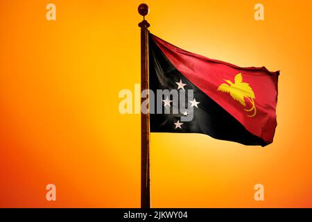 The national flag of Papua New Guinea on a flagpole isolated on an orange background Stock Photo