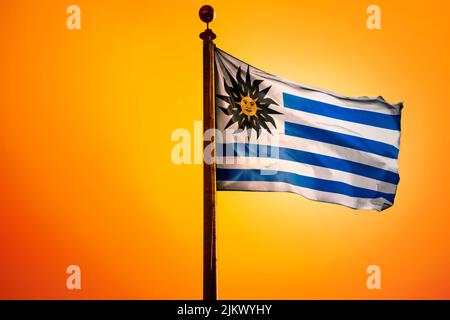 A 3D rendering of a waving flag of Uruguay on a pole on an orange background Stock Photo