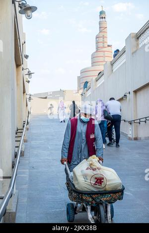 Coup de feu vertical d'un ouvrier poussant un chariot et des gens à Souq Waqif, un marché à Doha, dans l'État du Qatar Banque D'Images