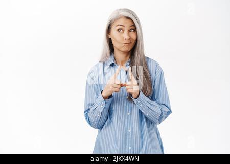 Image d'une femme asiatique mignonne qui a l'air innocente et timide, debout sur un arrière-plan de studio blanc Banque D'Images