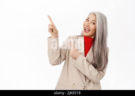 Portrait d'entrepreneur principal souriant, femme d'affaires pointant le doigt vers la gauche sur le produit, montrant une bannière publicitaire, debout sur fond blanc Banque D'Images