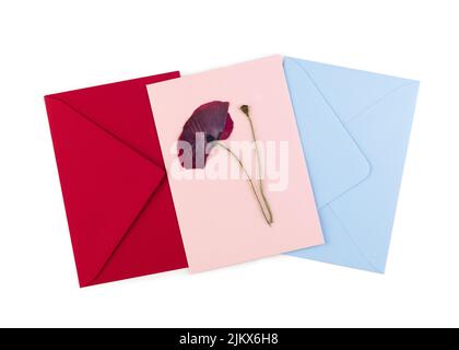 Une carte postale rouge de fleur pressée séchée et des enveloppes bleues et roses. Carte de vœux faite à la main en technique oshibana. Vue de dessus. Banque D'Images