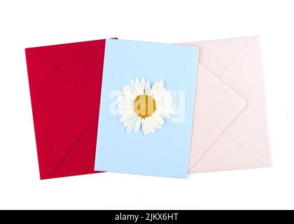 Une carte postale rouge de fleur pressée séchée et des enveloppes bleues et roses. Carte de vœux faite à la main en technique oshibana. Vue de dessus. Banque D'Images