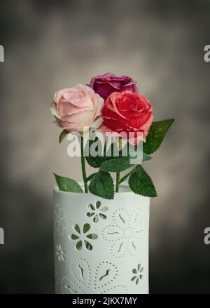 A vertical shot of three beautiful roses of different colors in a white ornamented vase Banque D'Images