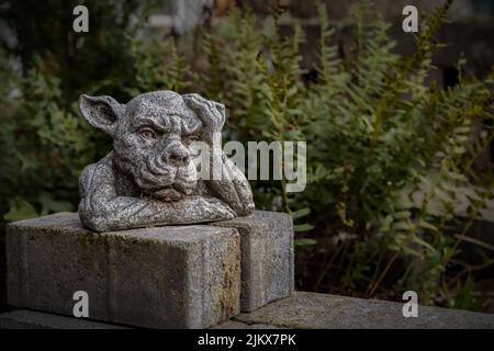 A closeup of a statue of a gargoyle or a gordon with its hand on the head in a park or garden Stock Photo