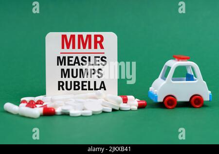 Concept médical. Sur une surface verte, une ambulance, des pilules et un signe blanc avec l'inscription - Measles-Mumps-Rubella Banque D'Images