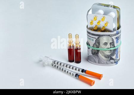 Les pilules, les ampoules et les seringues sont enveloppées dans des billets de dollars, fixés avec une bande élastique sur un fond blanc. Hausse des prix des médicaments et des produits pharmaceutiques m Banque D'Images