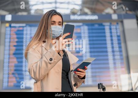 Jeune femme en masque tenant un smartphone à l'aéroport Banque D'Images